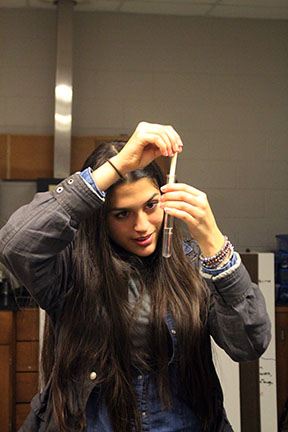 Examining her spit in the test tube, sophomore Minna Ramirez pulls her spit out that is attached to the rod.