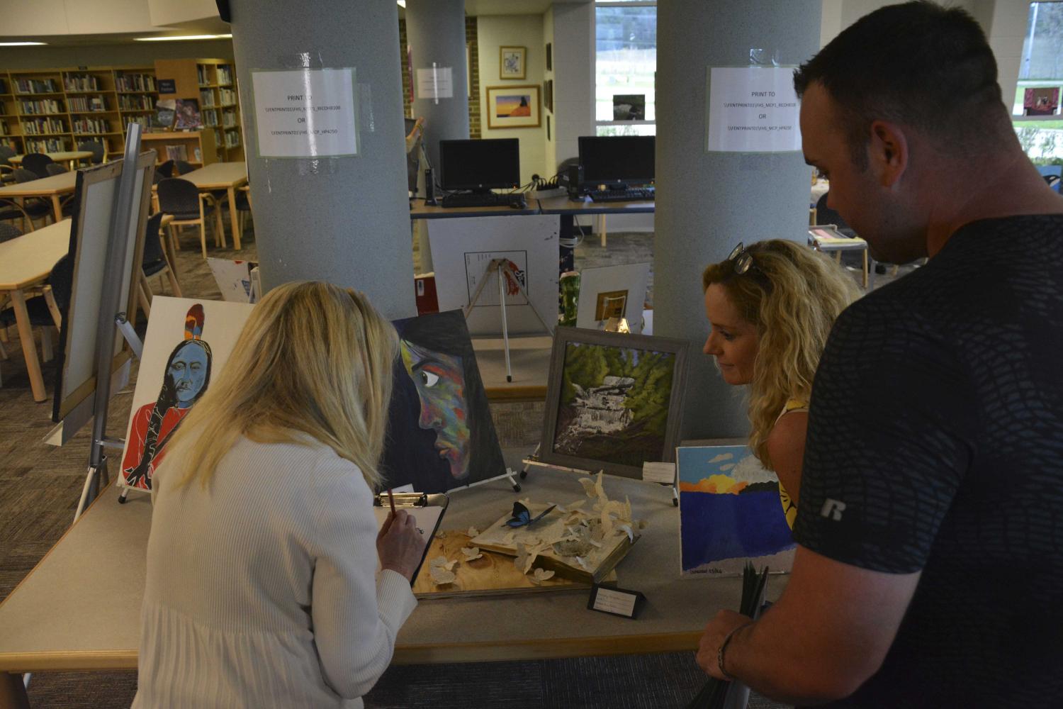 The judges evaluate the work displayed in the media center for the high school art show on April 27.