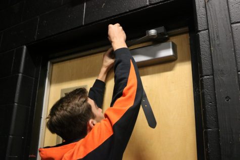During a lock down drill on Thursday Oct. 19, sophomore Ricky Giltrop puts a belt on the door hinge to help barricade the door. Barricading the door is a portion of the new lock down procedures.  