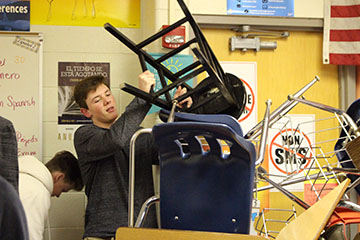 Stacking the chairs and desks, freshman Logan Angel participating in the lock-down drill in Mrs. Smelis class. After the drill Angel and his classmates put all desks and chairs back and got back to work.  