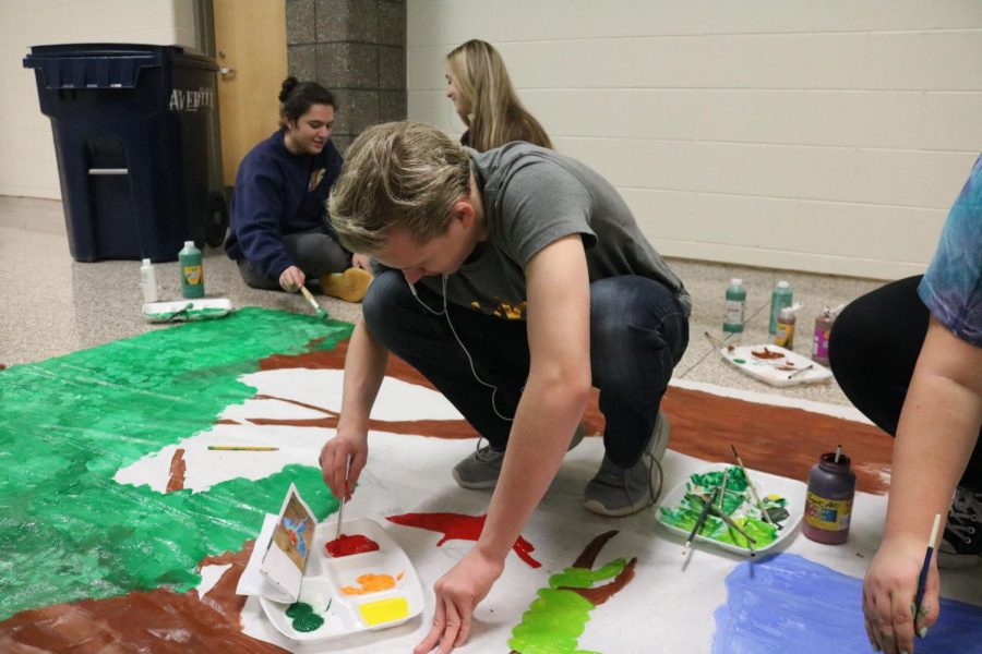 Painting a background drop for spirit week, sophomore Jake Kennedy takes time out of his SRT to help photo staff paint the background. Kennedy and the photo staff hung up the background by the cafeteria for students. teachers, and any staff members to take pictures at during lunches.