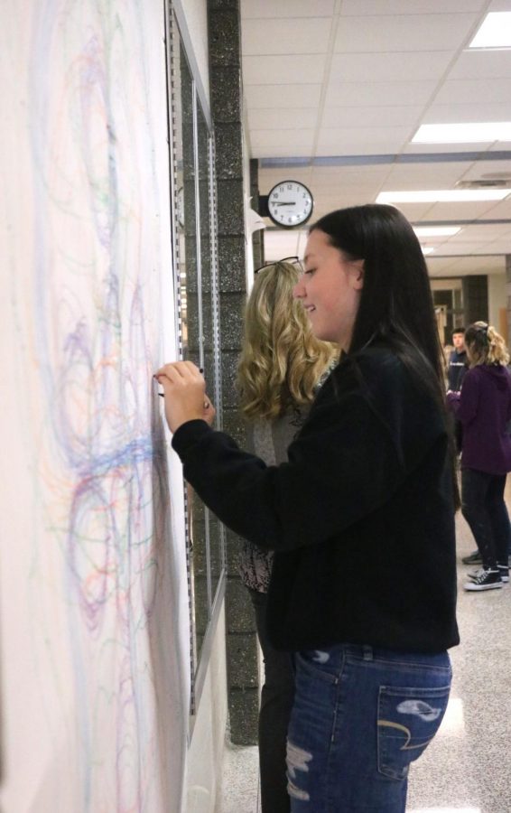 Sophomore Riley Hurley draws a symmetrical art piece with crayons on May 21. Students in art teacher Teresa Moss art class worked on art pieces taped to the wall. 
