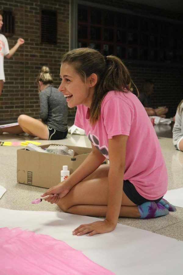 Dipping her paintbrush into the pink paint, freshman Laura Singer draws on the white poster. The cheerleaders decorated the Fenton High hallway on the night before homecoming. 

