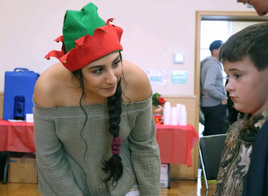 With an elf hat on, senior Zena Alshomali starts a conversation with a little boy who is waiting to see Santa Claus. Brunch with Santa was an annual event that is held in the Fenton Community Center.