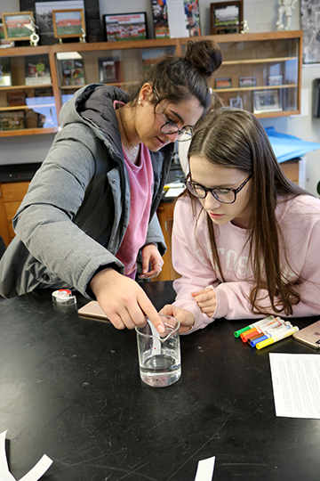 As they begin their lab, seniors Alaina Combs and Delaney Miesch dip paper into a beaker full of water. The Forensics students used markers and M&Ms to complete their labs.