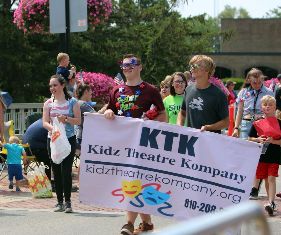 Juniors Jake Gurnsey and Lane Chodacki walk their Kidz Theatre Kompany banner in the Fourth of July parade. On July 4, students were welcome to walk or ride on the floats to show support for their activities. 