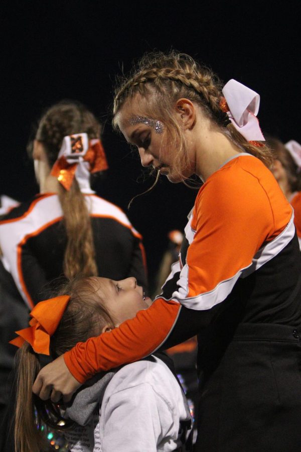 Sophomore Chloe Murray embraces her step sister and shows her how to cheer. The girls then watched the Fenton Tigers football team score, they cheered them on after the team got the point.