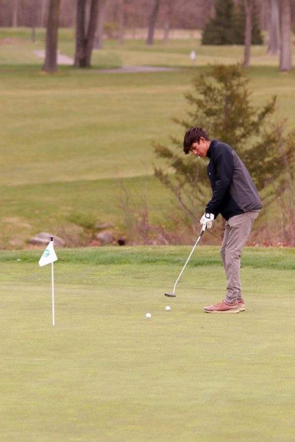 Practicing putting, junior Ethan Bright watches his ball go toward the hole. On April 26, the varsity boys golf team practiced before their match vs Corunna, and later won 222-182.