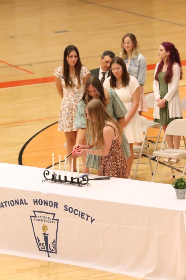 Junior Adrie Staib assists junior Lauren Gadola in lighting a candle representing one of the five pillars of the National Honor Society. On May 5, next years National Honor Society officers began the induction of the class of 2024 by lighting candles. 