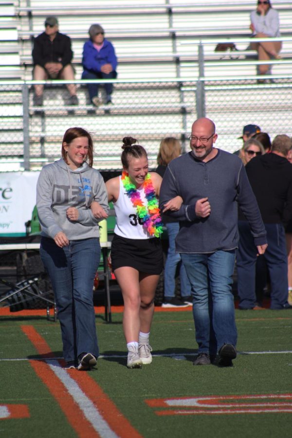 Laughing with her parents, senior Jordyn Bliss walks across the football field. On May 4, girls varsity lacrosse celebrated senior night. 