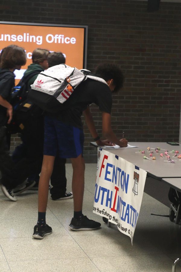 Junior Fisher Lane goes to the Fenton Youth Initiative table located in the square and signs the sign up paper. On Sept. 8, the leaders of the Fenton Youth Initiative club set up a table in the FHS square and handed out candy to students interested in joining.