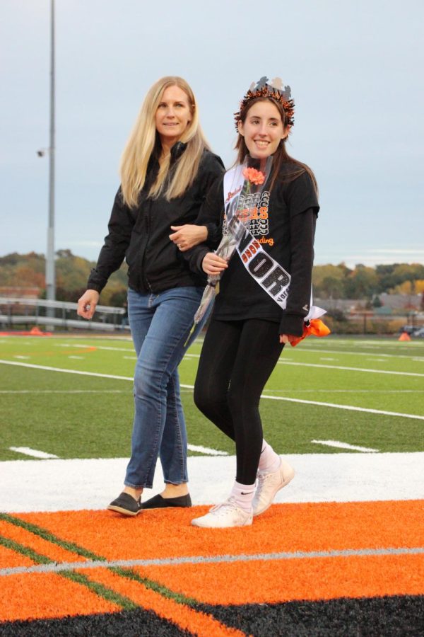Preparing for a picture, senior Selah Pescarolo walks down the field with her mom. On Oct. 14 senior night took place before the Fenton Varsity football game. Both cheerleaders and football players participated in that event. 