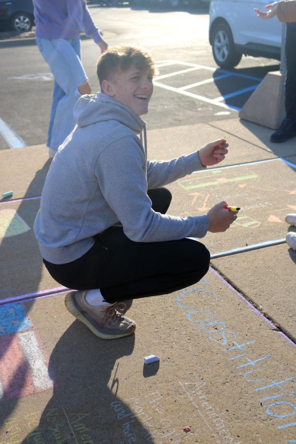 Laughing, junior Jake Nichols draws on the ground with chalk. On Oct. 5, government teacher Shawn Lawrences class drew vocab words outside on the sidewalk. 