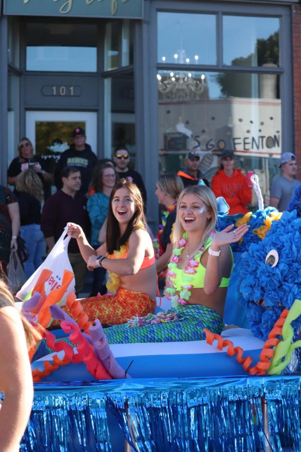 Sitting on a float, seniors Emily Mrazik and Madelynn Hyten laugh and wave to the crowd. On Sept. 30, the senior class of 2023 participated in building a float for the homecoming parade with the theme of Under the Sea.