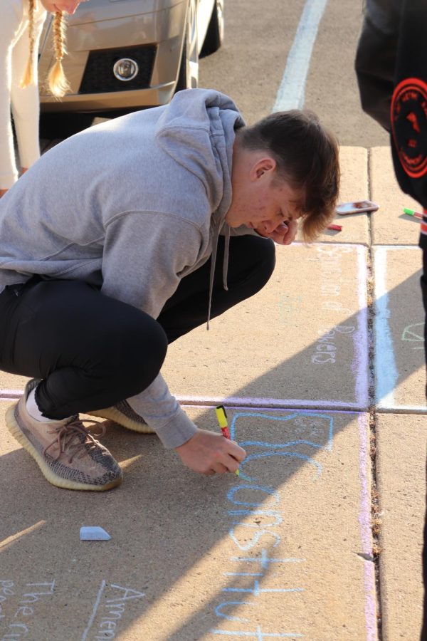 Drawing with chalk, junior Jake Nichols writes Constitustion on the sidewalk. On Oct. 5, government teacher Shawn Lawreneces class wrote vocabulary words.