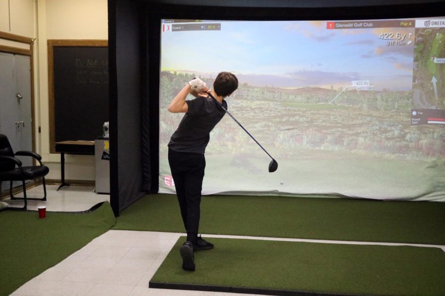 Junior Miles White hits his first drive of the day. On Feb. 8, the Fenton boys golfs respective members practice on their golf simulator in preparation for spring.