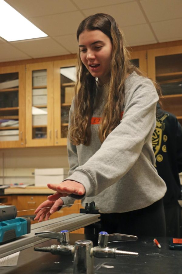 Pushing the cart, junior Paige Bakker test the friction on the track. On Feb. 7, science teacher Jason Kasaks physics class conducts a lab measuring the amount a friction compared to the weight of the cart.