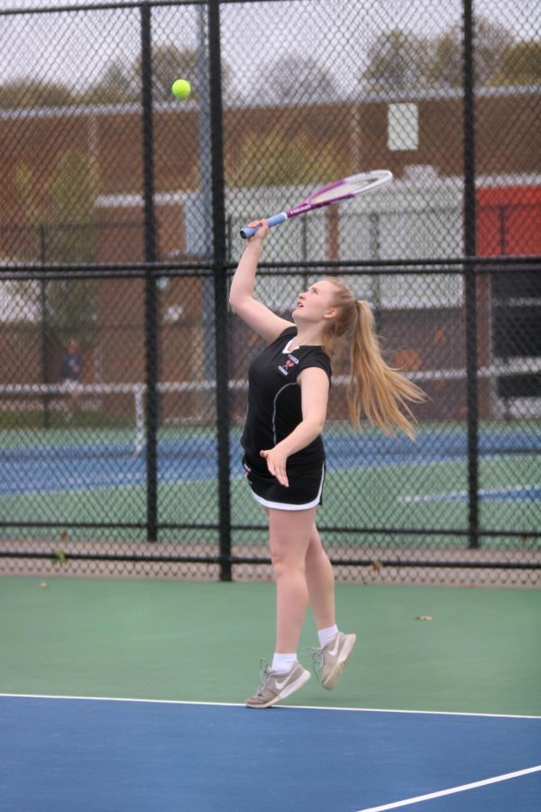 Swinging, junior Carli Best attempts to serve. On May 8, the girls varsity tennis team beat Owosso. 