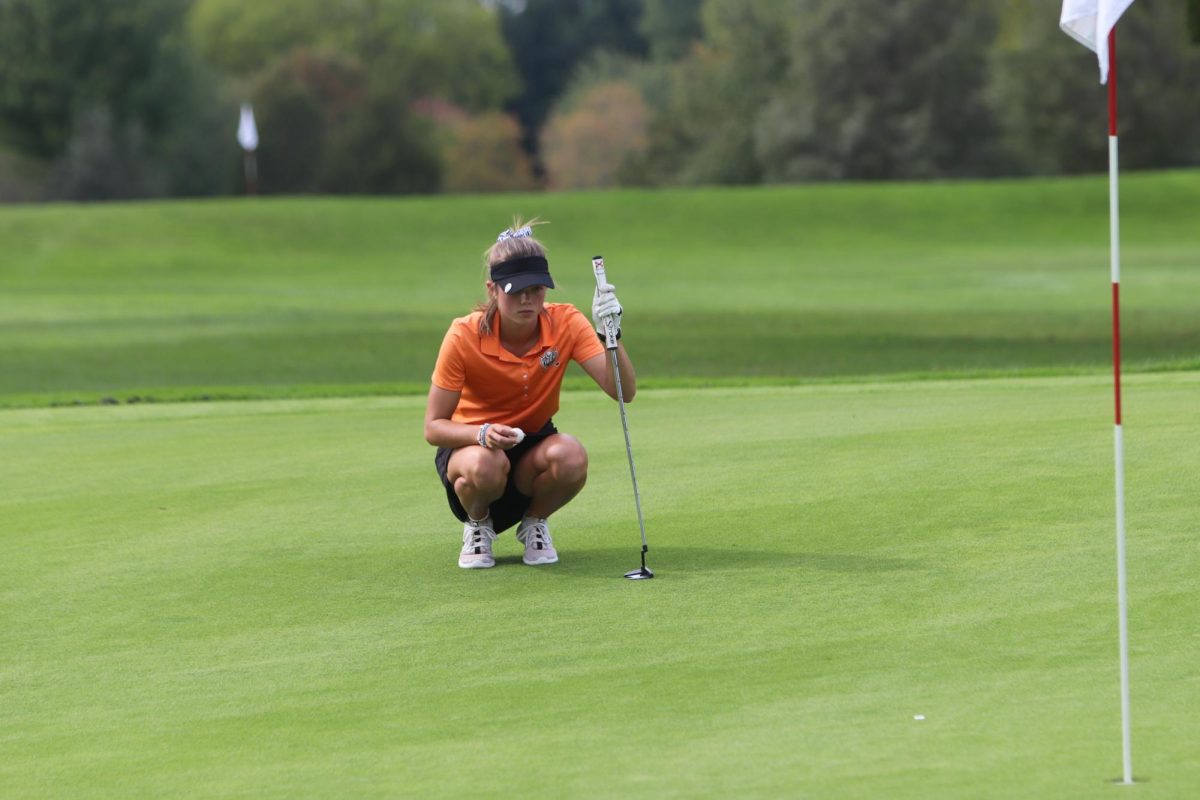 Lining up her putt, junior Payton LaRowe kneels down to place her ball on the green. On Sept. 19, Fenton girls varsity golf had a match against Flushing winning 189-217.