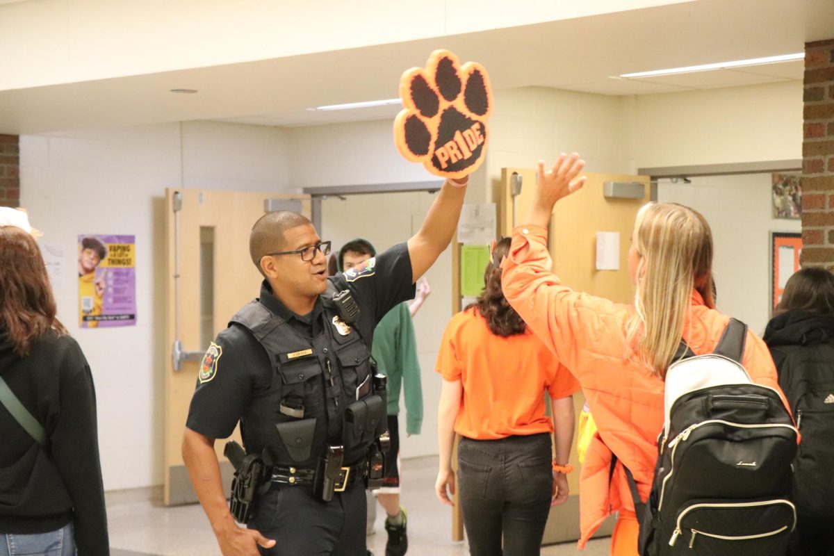 Raising his hand, Officer Jordan Grace gives out high fives before school. On Oct. 6, students and staff showed their spirit by wearing orange and black for homecoming.