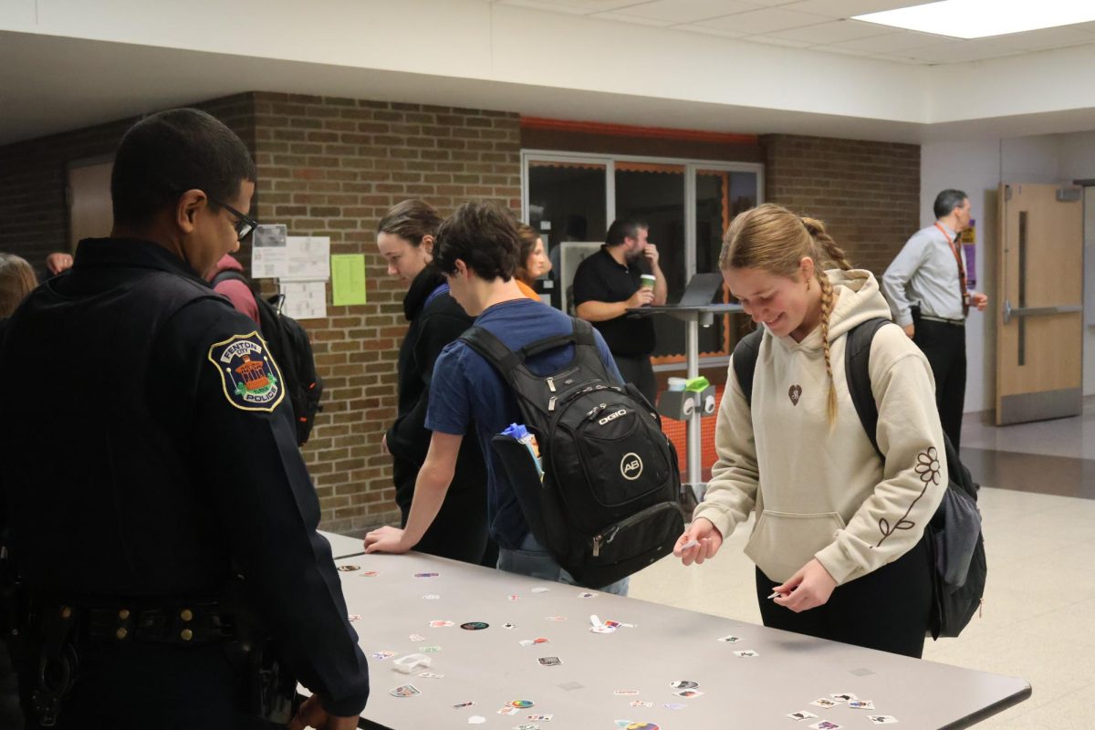 Smiling, junior Zoe Plunkett reaches for a sticker. On Oct. 26, students had the opportunity to receive stickers while walking into school in the morning.