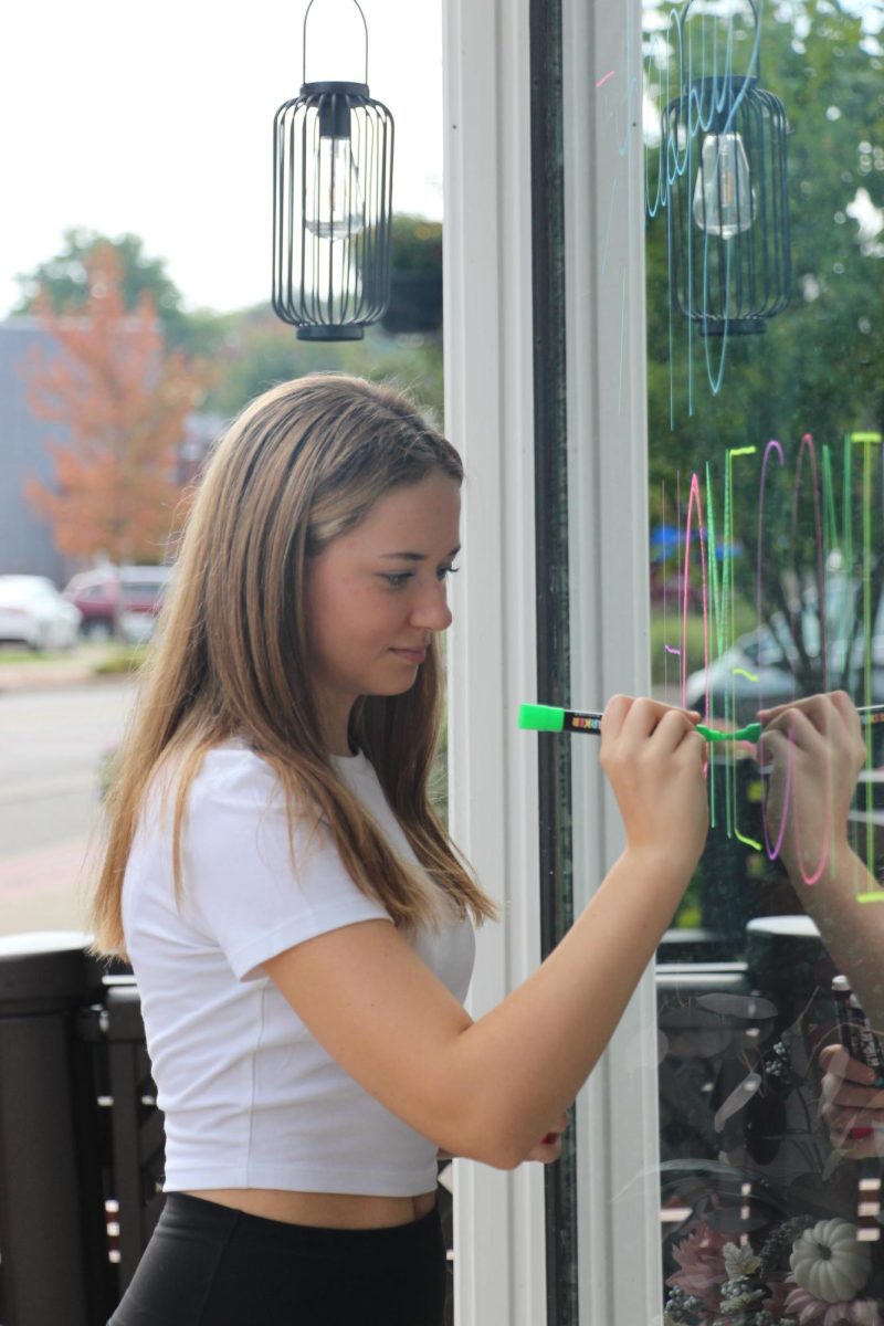 Writing, senior Emma Minock draws on the window. On Oct. 1, Student Council participated in Paint the Town in order to prepare for Homecoming. 