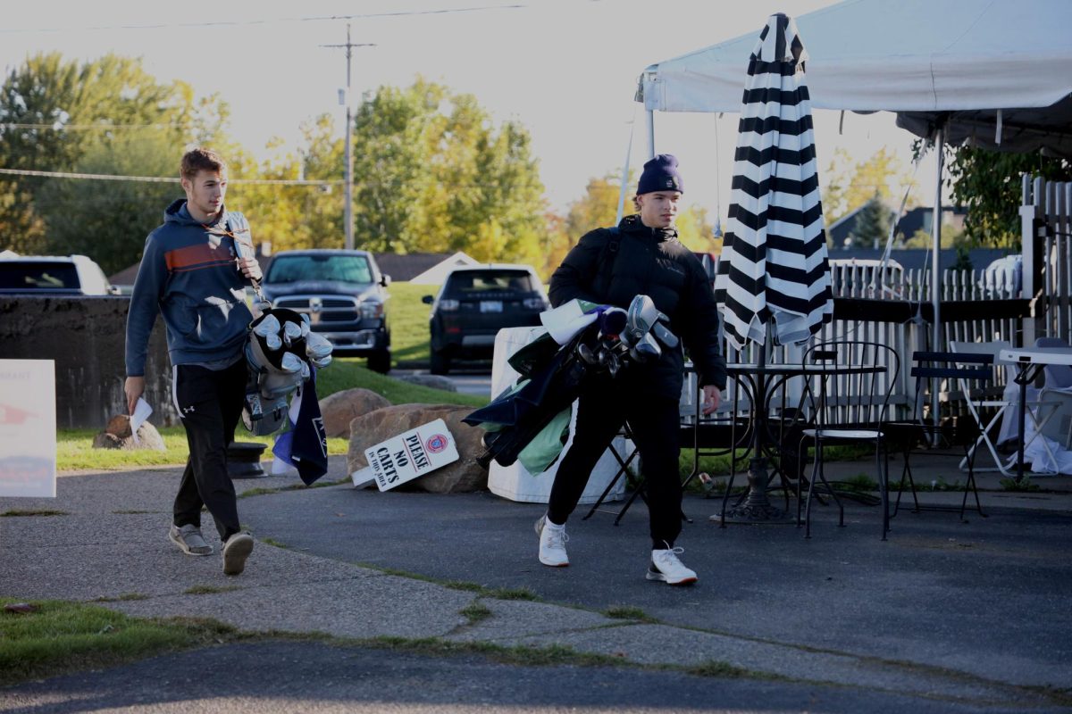 Helping out at their fundraiser, junior Levi Hudson and senior Hank Wojtaszek are carrying golf bags. On Oct. 8 the Fenton boys golf team held a fundraiser outing at Fenton Farms Golf Club.