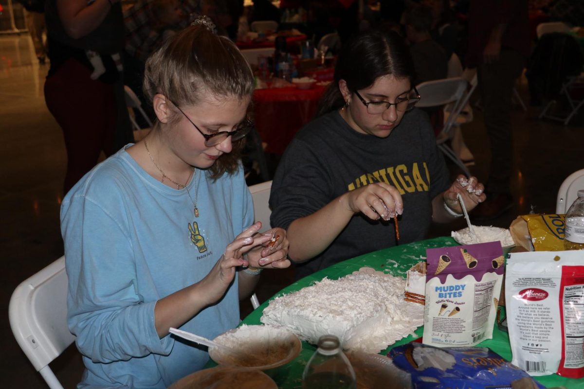 Decorating, Junior Addison Browne and sophmore Hayley Jensen create their gingerbread ski lift. On Dec. 8, the Rock Church held a gingerbread house decorating contest.