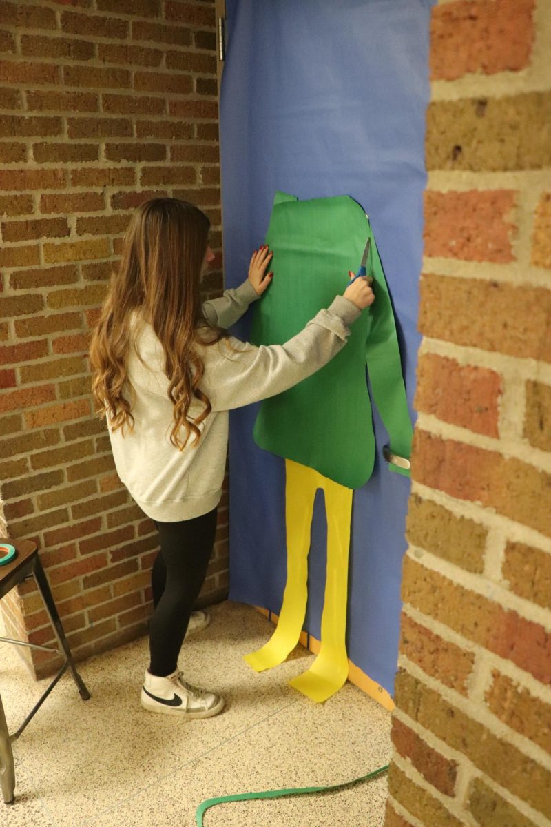 Cutting the paper, senior Sunny Wilkinson finishes cutting out the body of the elf. On Dec. 5, some of the SRT classes participated in the door decorating challenge.