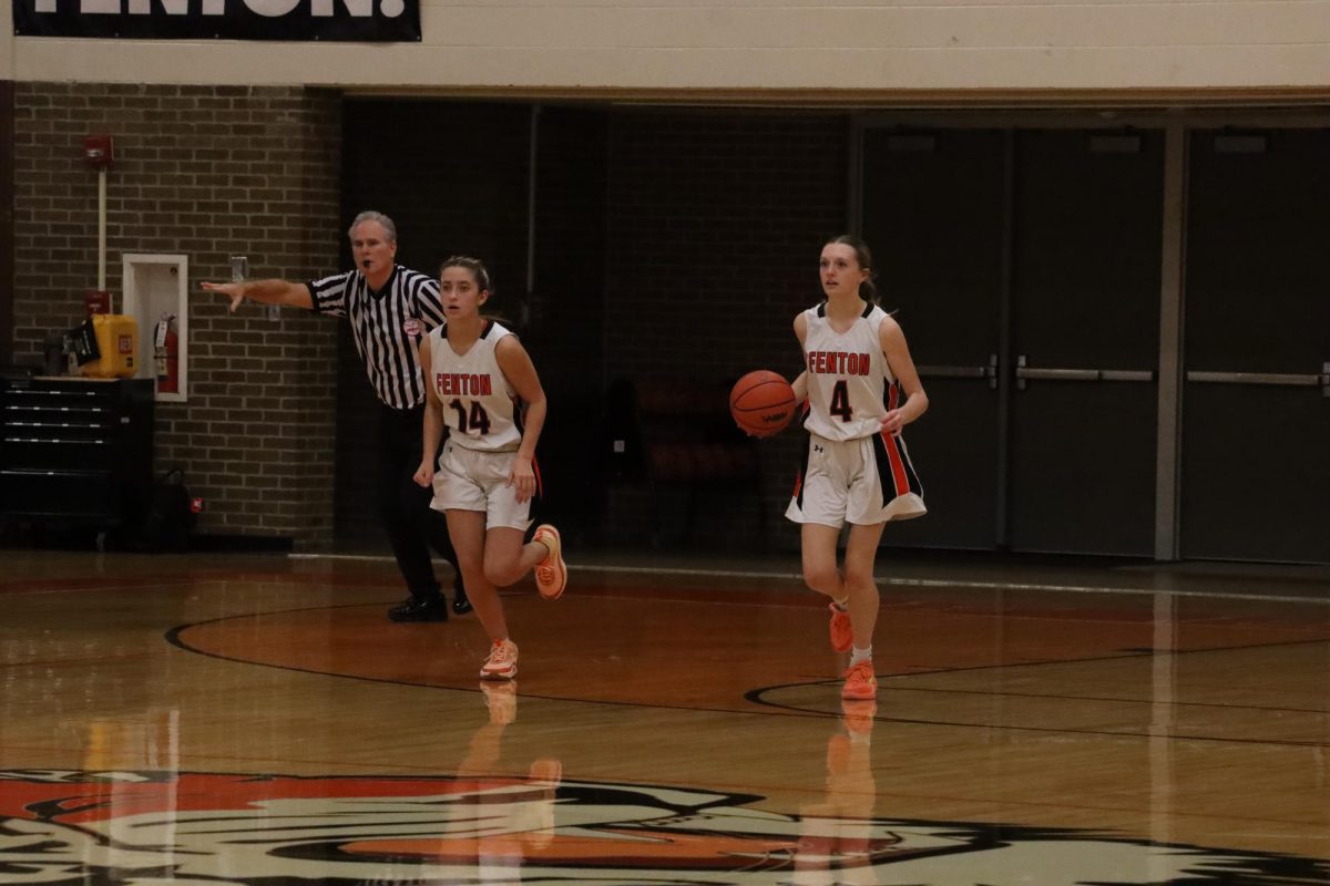 Dribbling down the court, freshman Natalie Hunault prepares to pass the ball to one of her teammates. On Jan. 8, the JV girls basketball team lost 24-25 to the Holly Bronchos.