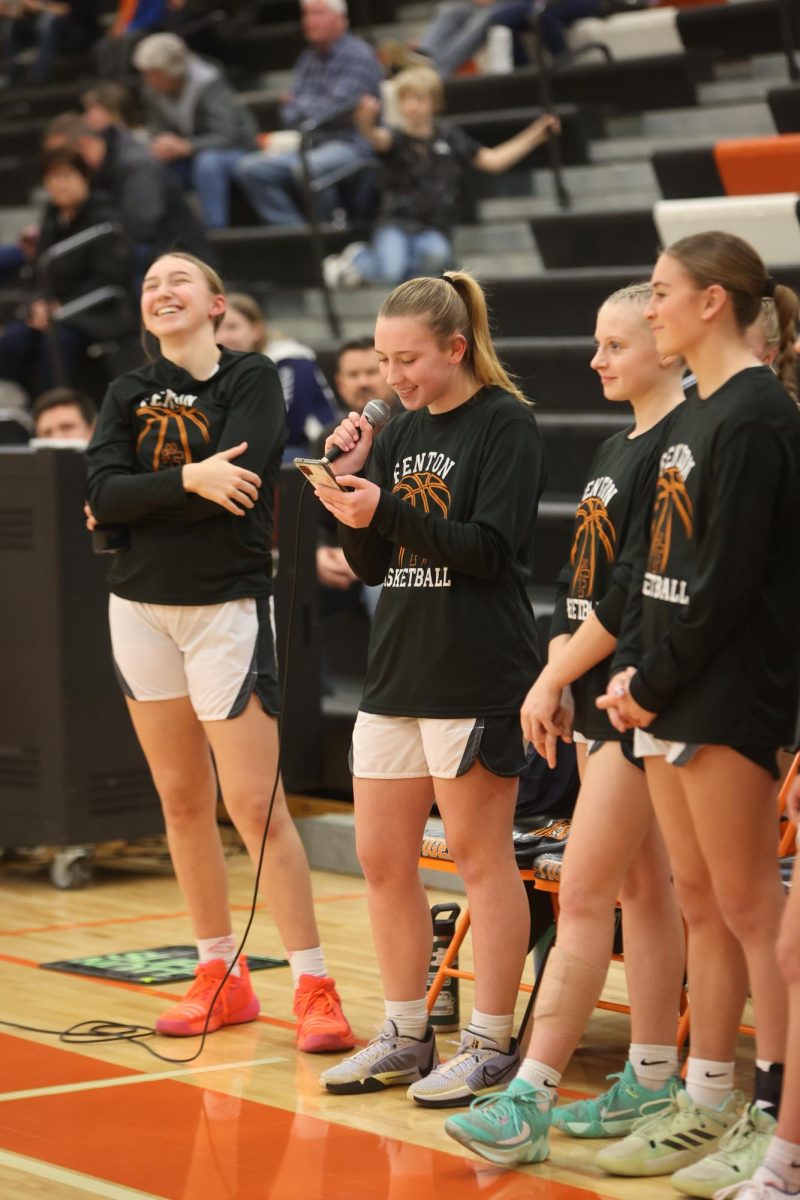 Reading her phone, sophomore Stella Nueveman talks into the microphone along side her teammates. On Feb. 9, the girls varsity basketball team hosts senior night. 
