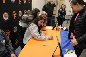 Smiling, senior Sophie Collins writes on a photo for a youth softball player. On Feb. 8, the Fenton softball teams got together to celebrate Sophie Collins with her signing.