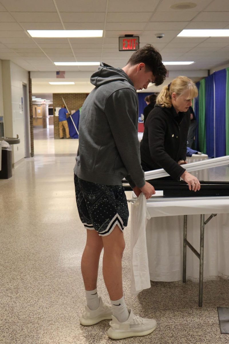 Standing, Freshmen Grant Hunault helps take off table covers. On March 3, the boy's basketball teams help take down decorations from the Fenton EXPO. 