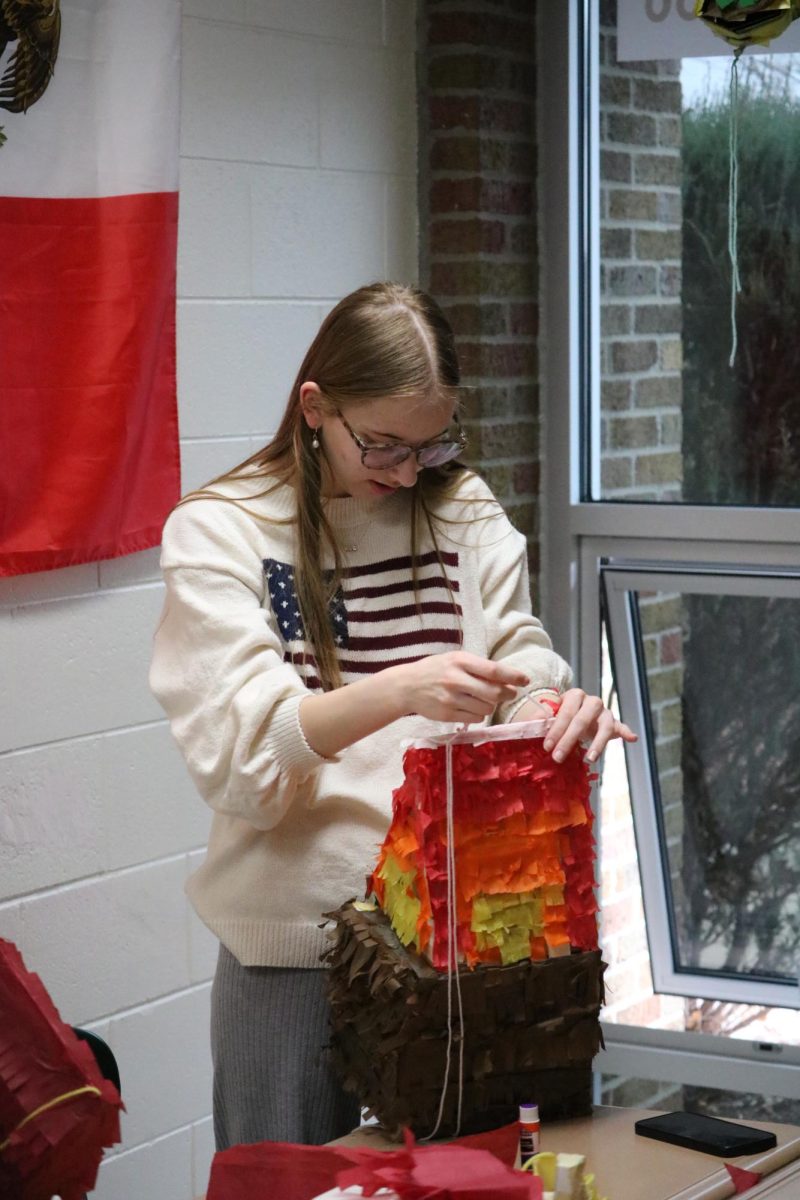 Gluing on a string, sophomore Cassie Harris adds the final touches to her pinata. On March 18, Mrs.Fischers spanish three class created pinatas to hang from the ceiling.  