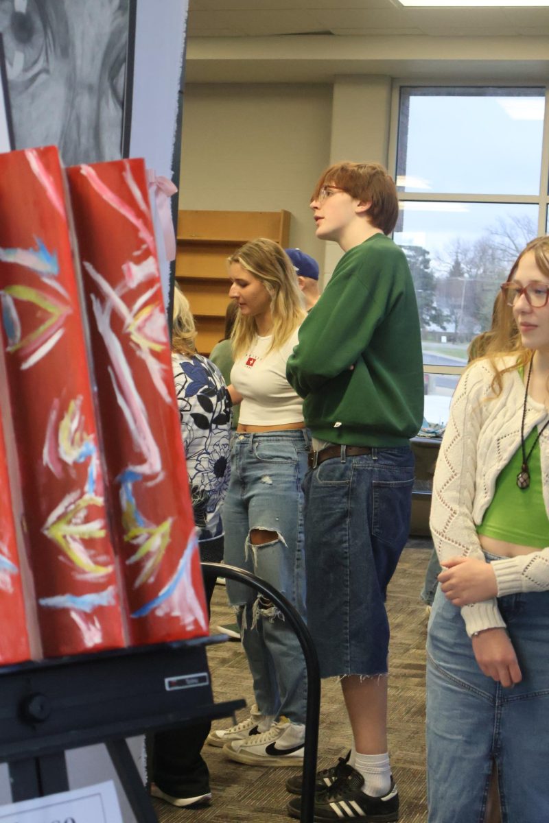 Observing, sophmore Simon Graff walks around the exhibit and views the art. On April 4, Mrs. Jambek hosted an art show for her current students.