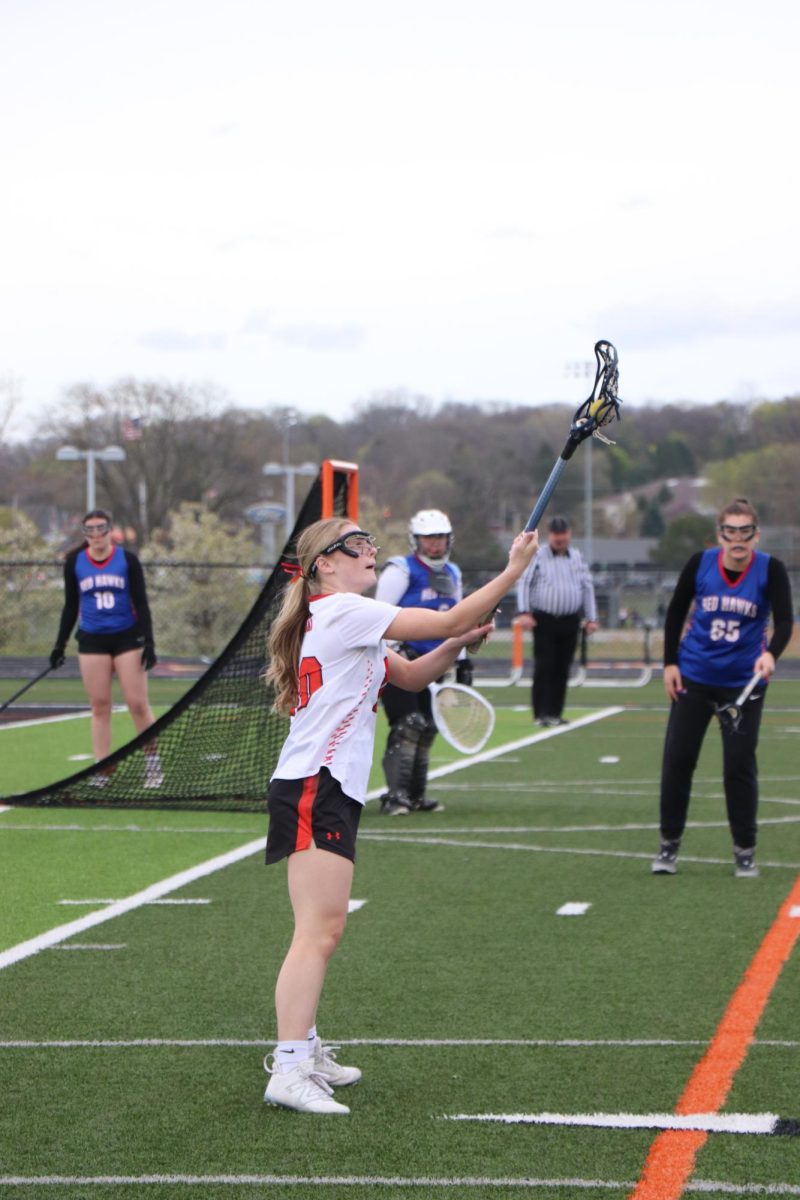 Holding the ball, sophomore Evie Metcalfe makes a catch. On Apr. 23, the varsity lacrosse team played Holly and lost 5-9.