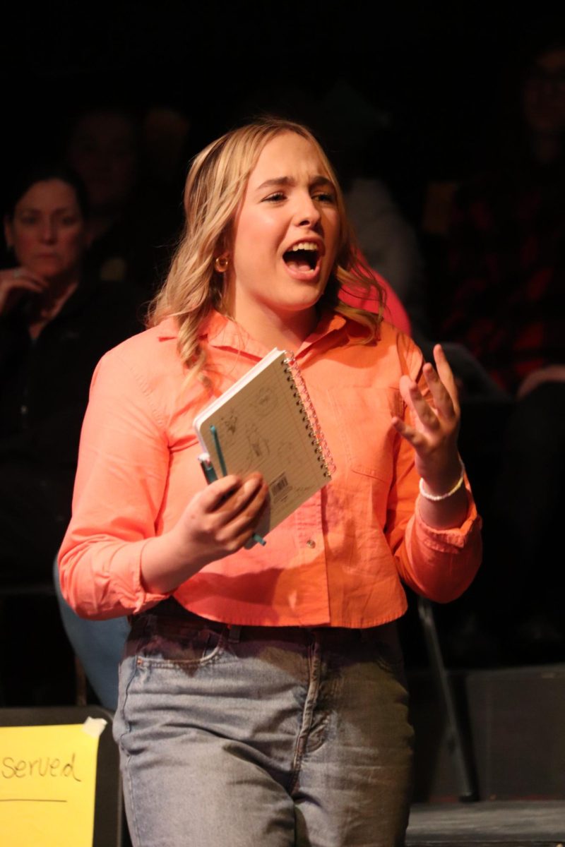 Speaking to the audience, junior Maya Bethke participes in a theater director Lori Thompsons last production before retirement. On April 12, the IB theater performed Every Brilliant thing in the black box. 
