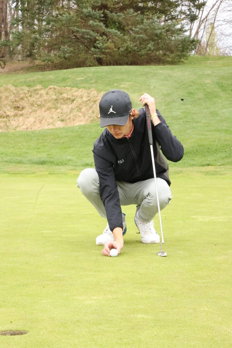Lining up his ball, senior Carter Will prepares for his putt. On April 23, the boys varsity golf team played Corunna and won 178-203.