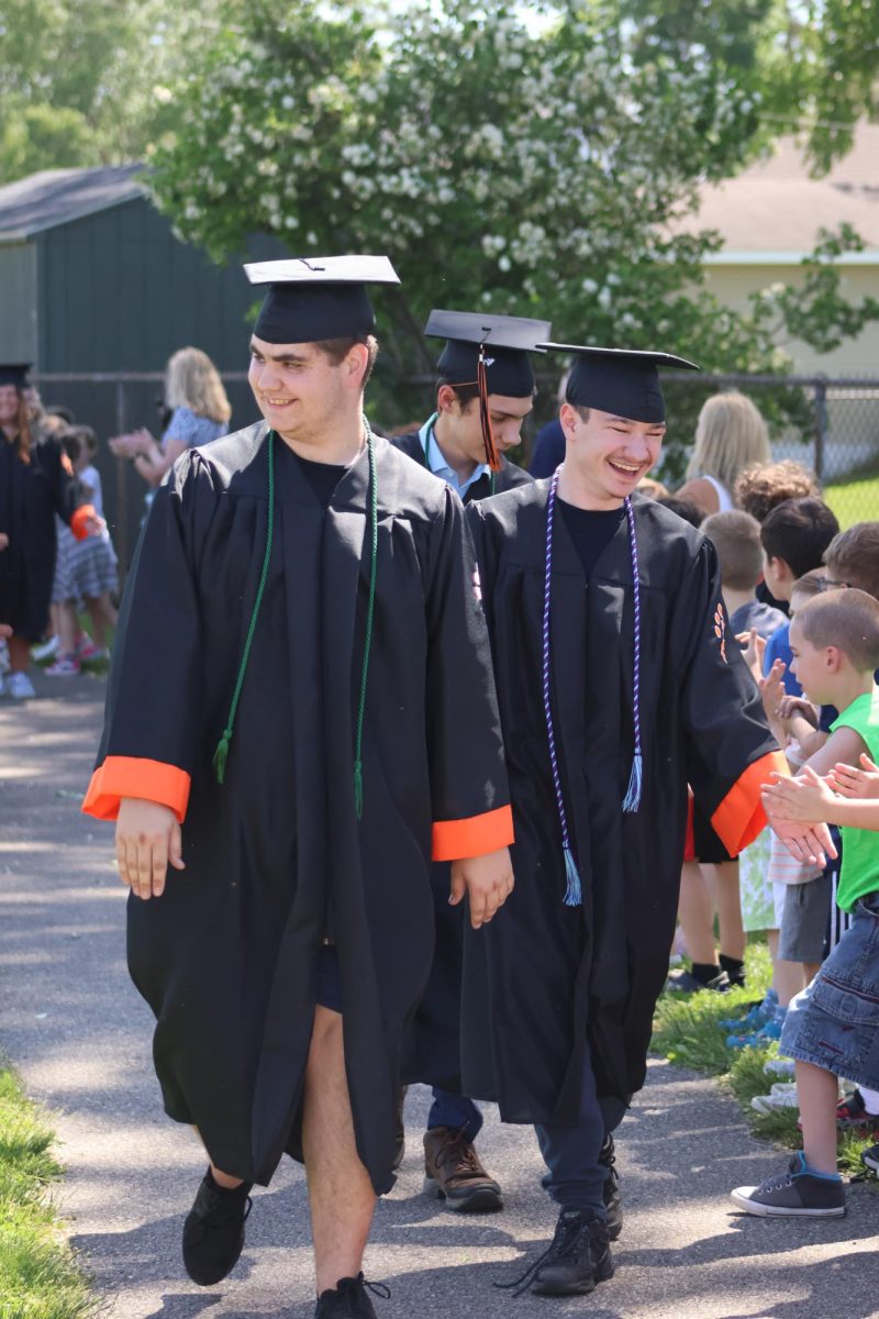 Smiling, seniors Alex Cook and Logan Davis participate in the North Road clapout. On May 22, the elementary students lined up along the track to clap for the graduating seniors.