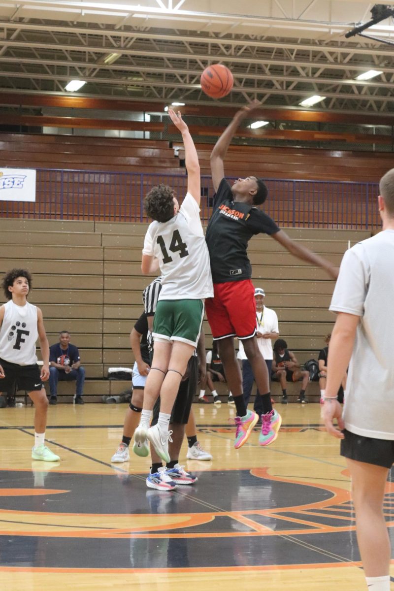 Jumping, sophomore Grant Hunault does jump ball to start the game. On June 25, the boy's varsity basketball team had a summer league game. 