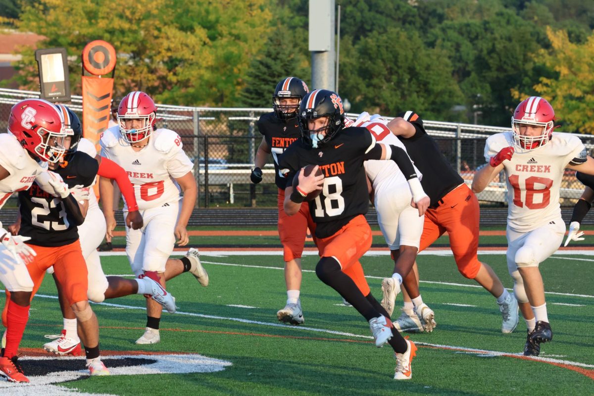 Sprinting past the defenders, freshman Rhys Sheil runs with the ball to score a touchdown. On Sept,12 the Fenton JV Tigers beat the Swartz Creek Dragons 43-22.