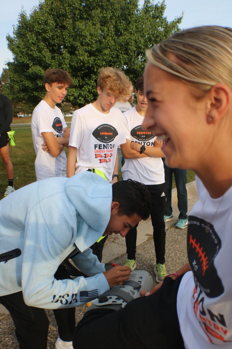 Laughing, sophomore Sage Menzies gets her boot signed by Olympian Grant Fisher. On Sept. 27, the cross country team held their annual ball run for homecoming where they ran the game ball from Kearsley High back to Fenton High.   