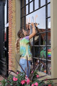 Painting in orange and black, senior Ariana Papcun paints the windows of businesses downtown to prepare for homecoming. On Sept. 22, members of student council painted the town for homecoming week.