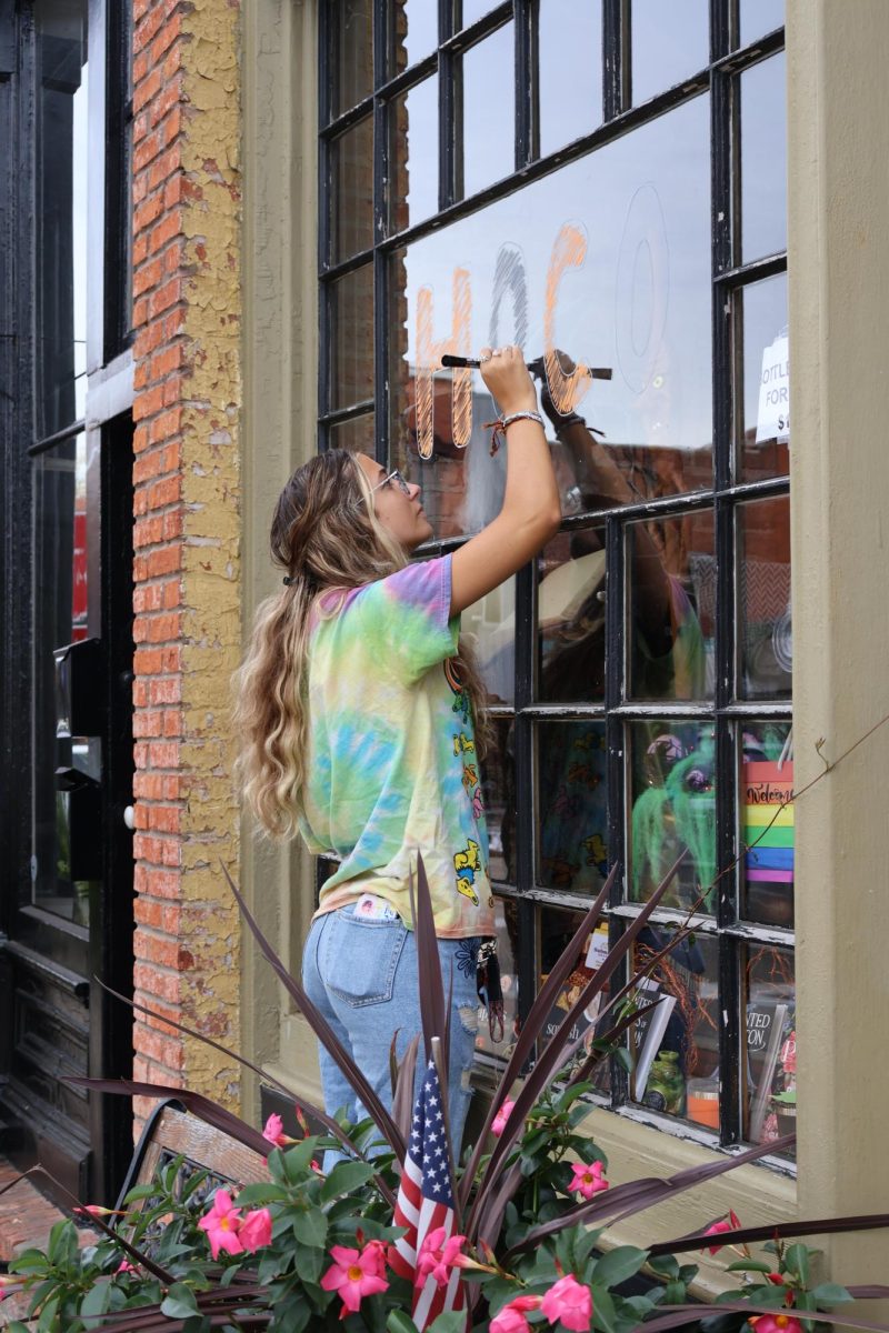 Painting in orange and black, senior Ariana Papcun paints the windows of businesses downtown to prepare for homecoming. On Sept. 22, members of student council painted the town for homecoming week.