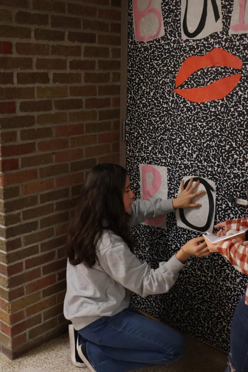 Taping a letter on the door, sophomore Janessa Bemman helps decorate her SRT door. On Sept. 17, students decorated their classroom doors in preparation for homecoming.    