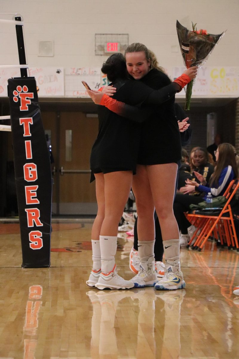 Smiling, senior Anna Logan and freshman Maggie Chanter hug after hearing speeches during senior night. On Oct. 9, the varsity volleyball team celebrated their 5 seniors.