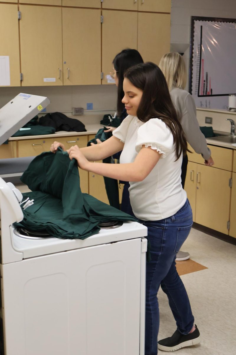 Preparing the shirt, senior Isabella Kozlesky is taking a shirt off the pile to put onto the screen printing machine. On Oct. 17, teacher Julie Montana's Tiger INC class printed shirts for the Fentonian staff.