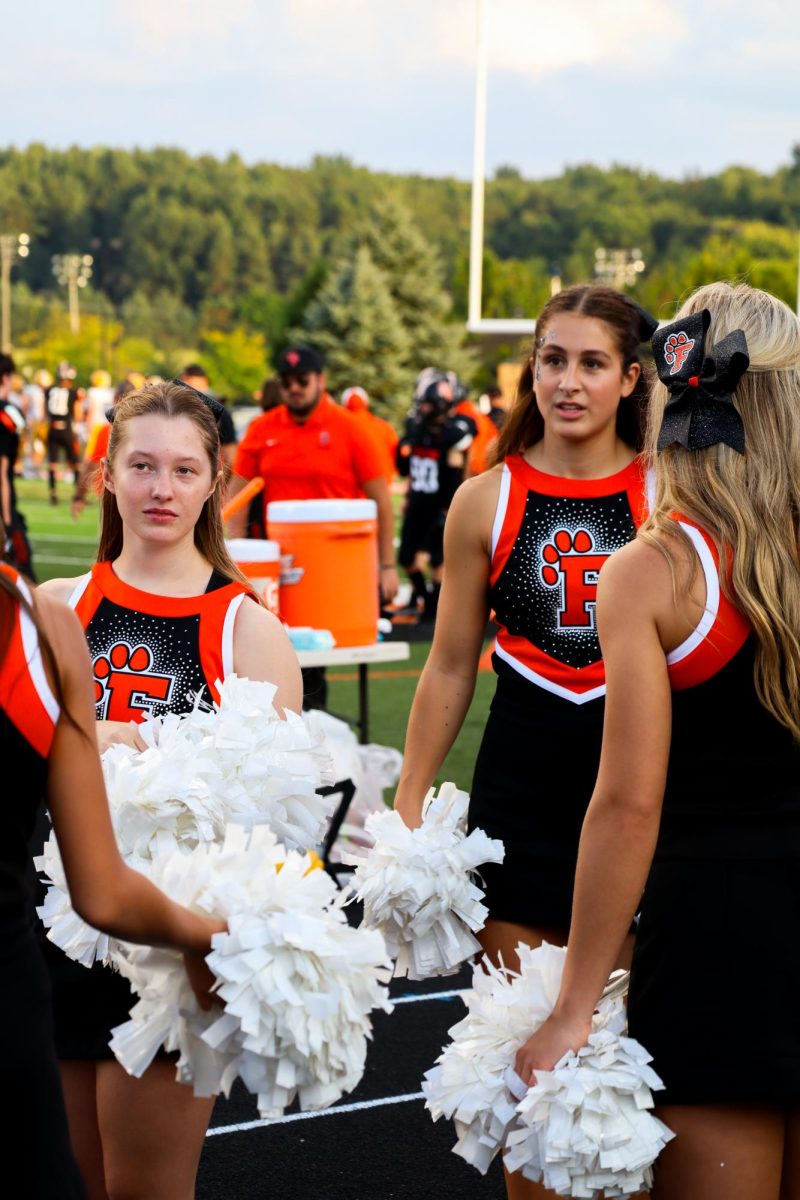 Preparing, sophomores Sophia Davidson and Campbell Dean discuss which cheer to perform next. On Aug. 28, Fenton varsity cheer encouraged the student section. 