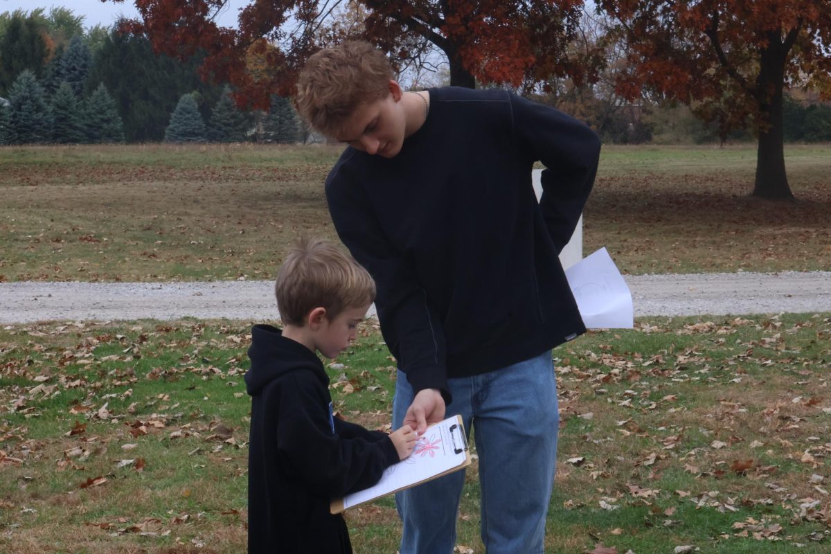 Helping, senior Sawyer Miller is teaching a first grader from North Road about a flower's structure. On Oct. 23, FHS students participated in our annual pond day. 