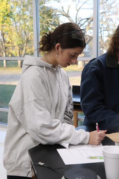 Writing on her paper, senior Paige Harrison works with her group. On Nov. 13, IB Chemistry had a lab to determine the change in temperature of different reactants. 